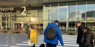 Frouck de Boer en Peter Waalboer aan het werk om de toegankelijkheid van Schiphol te verbeteren voor mensen met een visuele handicap. Ze staan buiten voor Vertrekhal 2 en bespreken een geleidelijn bij een voetgangersoversteekplaats